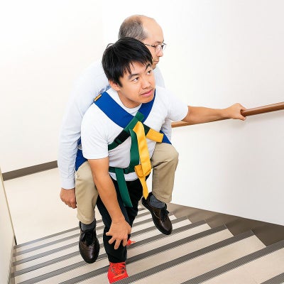 男性がおんぶ担架で男性利用者を階段で運んでいる